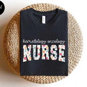 Puede incluir: Camiseta negra con el texto "hematology oncology NURSE" en blanco con detalles florales.