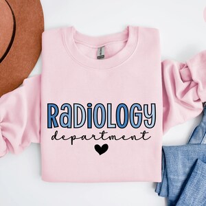May include: Light pink sweatshirt with the text "RADIOLOGY department" in blue gradient lettering and a black heart.