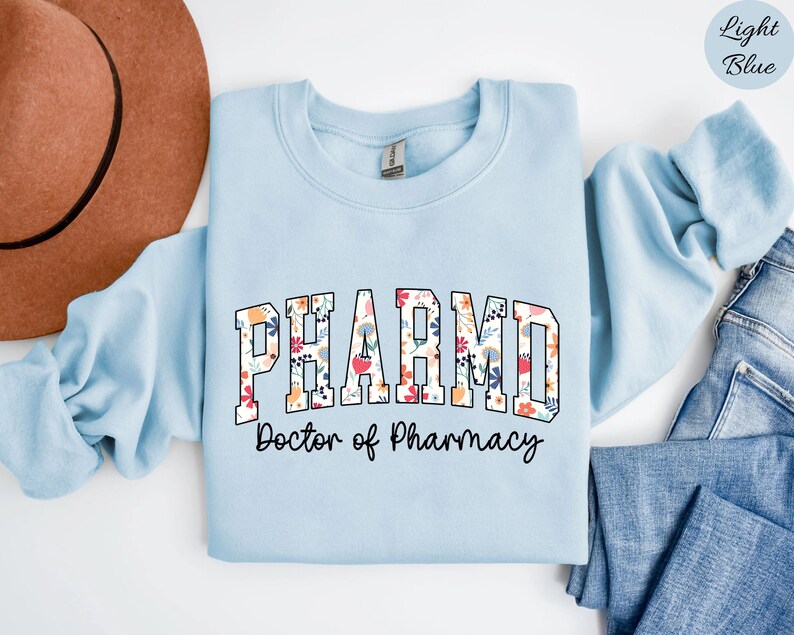 May include: Light blue sweatshirt with a floral print design that says "PHARM.D. Doctor of Pharmacy" in black text.