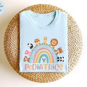 May include: A light blue t-shirt with a rainbow and animals printed on the front. The text "PEDIATRICS" is printed below the rainbow.