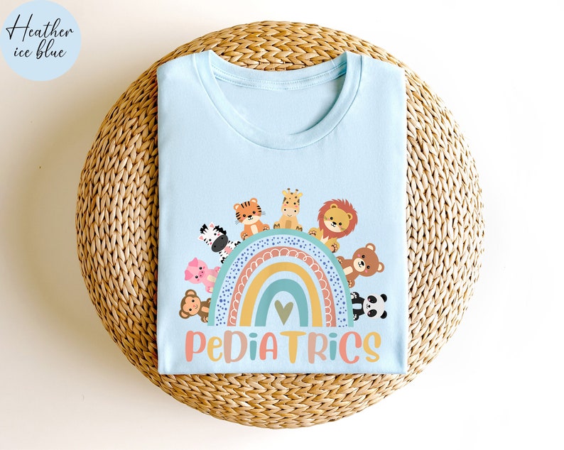 May include: A light blue t-shirt with a rainbow and animals printed on the front. The text "PEDIATRICS" is printed below the rainbow.