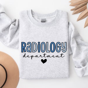 May include: A gray sweatshirt with the text "Radiology department" in blue and black lettering with a small black heart. The sweatshirt is on a white background.