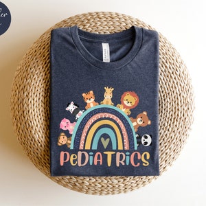 May include: A dark heather navy blue t-shirt with a rainbow and cute animal graphic. The text "PEDIATRICS" is printed below the rainbow.