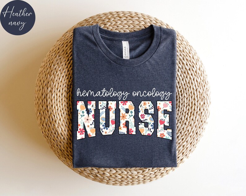 Puede incluir: Una camiseta azul marino jaspeada con el texto "hematolog&iacute;a oncolog&iacute;a ENFERMERA" en letras blancas con un patr&oacute;n floral.