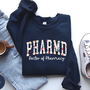 May include: Navy blue sweatshirt with a floral design and the text "PHARM.D. Doctor of Pharmacy".