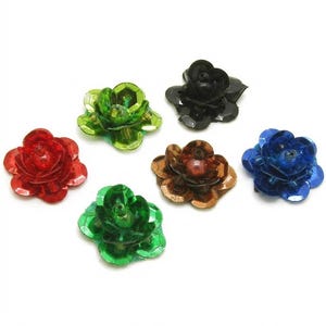 Puede incluir: Un conjunto de seis adornos en forma de flor hechos de lentejuelas superpuestas, translúcidas y opacas, en colores rojo, verde claro, negro, verde oscuro, marrón y azul. Cada pieza presenta una cuenta central y un diseño floral.