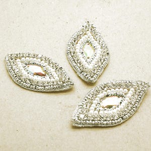 May include: Three marquise-shaped embroidered patches featuring a central iridescent crystal surrounded by a ring of small white beads and an outer border of clear rhinestones set in silver-toned metal, creating a decorative embellishment.