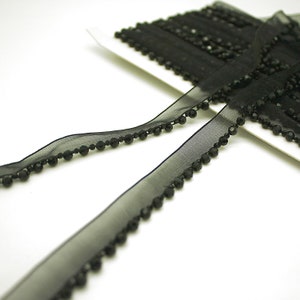 May include: Black beaded trim with a sheer black ribbon. The trim is made of small black beads sewn onto a black ribbon.
