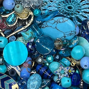 May include: A collection of blue and turquoise beads and embellishments. The assortment includes various shapes and sizes, such as round, teardrop, and star-shaped beads, along with decorative elements. The color palette ranges from light to dark shades of blue.