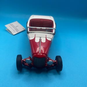 Puede incluir: Un coche de juguete vintage rojo y blanco con neumáticos negros. El coche tiene techo e interior blancos, con carrocería roja. El coche tiene dos faros y un parachoques cromado. El coche de juguete es un objeto de colección clásico.