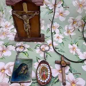 May include: Religious items including a wooden crucifix with a metal Jesus figure, two keychains with religious images, and a wooden cross pendant on a black cord. The items are on a floral background.