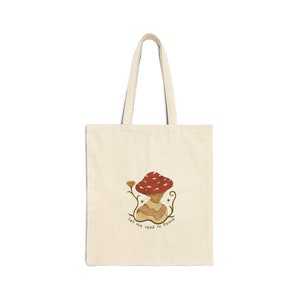 Könnte beinhalten: Eine beige Einkaufstasche mit einer Pilzillustration und dem Text "Let me read in peace".