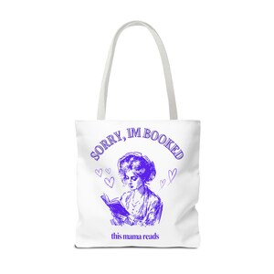 Könnte beinhalten: Weiße Einkaufstasche mit einem violetten Design. Das Design zeigt eine Frau, die ein Buch liest, mit dem Text "SORRY, IM BOOKED" in einem Kreis um sie herum. Unter dem Design steht der Text "this mama reads".