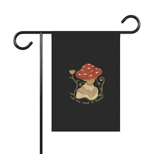 Puede incluir: Una bandera de jardín negra con una ilustración caprichosa de una persona que lleva un sombrero de hongo rojo y el texto "Déjame leer en paz".