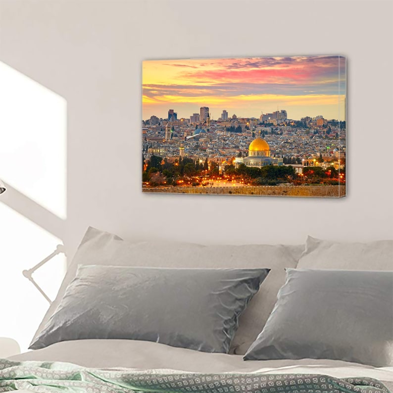 May include: A panoramic view of Jerusalem at sunset, with the Dome of the Rock, a golden dome, in the foreground. The city is spread out below, with buildings and trees visible. The sky is a mix of pink, orange, and purple.