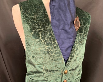 May include: A green velvet vest with a cracked pattern and gold buttons. The vest has a pocket on the left side and is worn over a blue cravat.