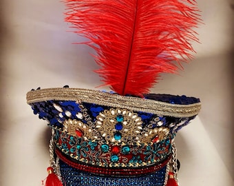 May include: A blue sequined hat with gold trim and red tassels. The hat is decorated with rhinestones and beads. A red feather is attached to the top of the hat.