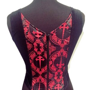 Op de afbeelding: Zwart, mouwloos top met een rood en zwart patroon van kruisen en sierlijke ontwerpen. Het top heeft een rits aan de achterkant.
