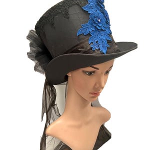May include: Black top hat with a wide brim, adorned with blue floral lace and a black tulle accent. The hat features a satin finish and is designed for special occasions or costume wear.