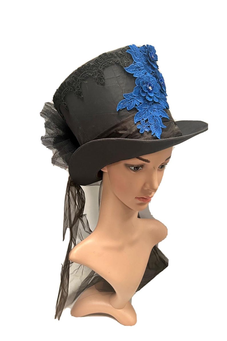 May include: Black top hat with a wide brim, adorned with blue floral lace and a black tulle accent. The hat features a satin finish and is designed for special occasions or costume wear.