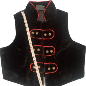 May include: Black velvet vest with a mandarin collar and red piping. The vest has five gold buttons down the front.