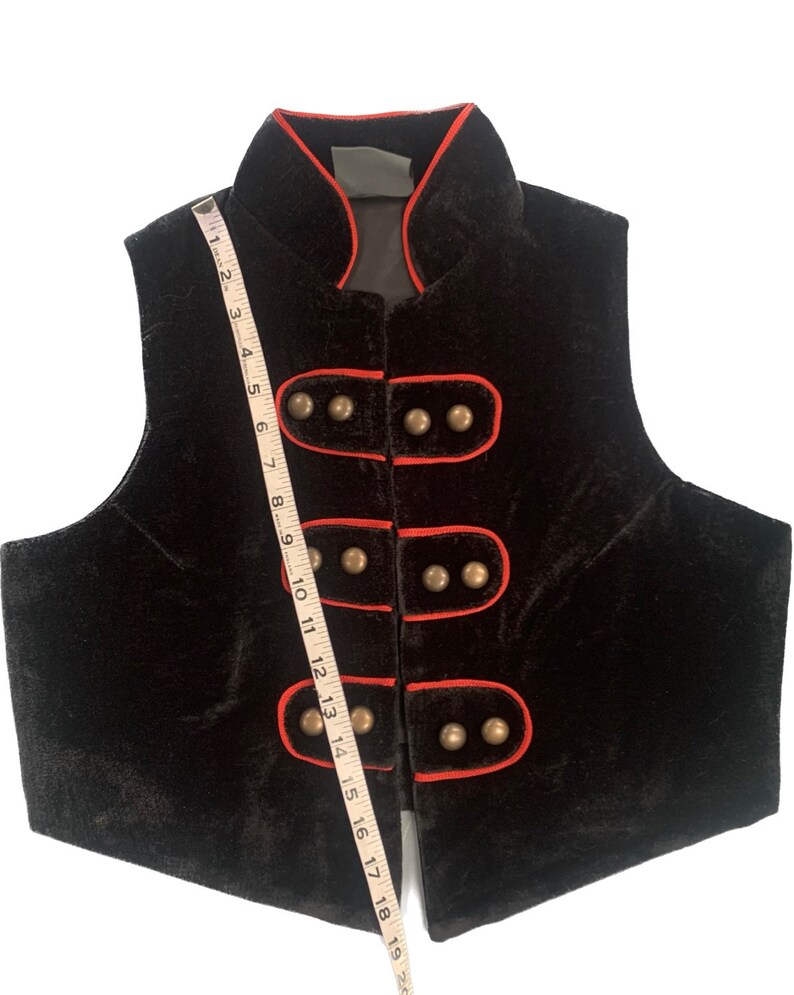 May include: Black velvet vest with a mandarin collar and red piping. The vest has five gold buttons down the front.