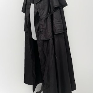 May include: A black cape with a layered collar and a flowing design. The cape is made of a textured fabric and hangs on a white mannequin. The garment has a classic, elegant style.