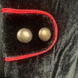 May include: Close-up of a black velvet jacket with red trim and two silver buttons.