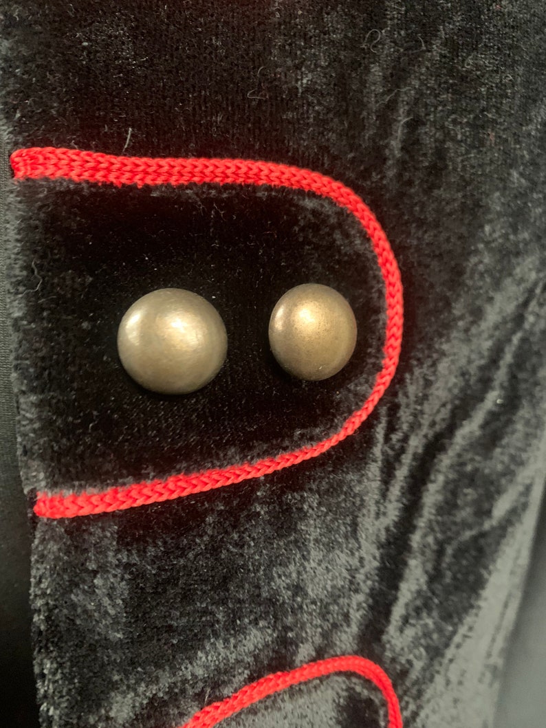 May include: Close-up of a black velvet jacket with red trim and two silver buttons.