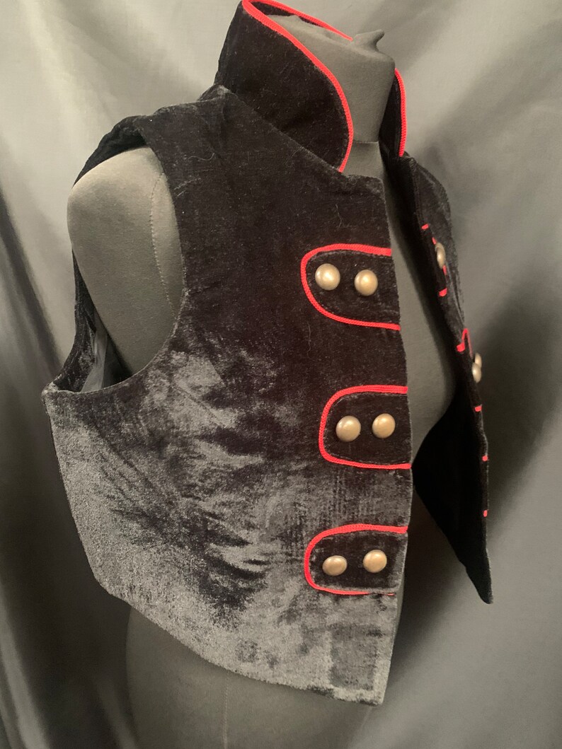 May include: A black velvet vest with a red trim and silver buttons. The vest has a stand-up collar and a fitted silhouette.