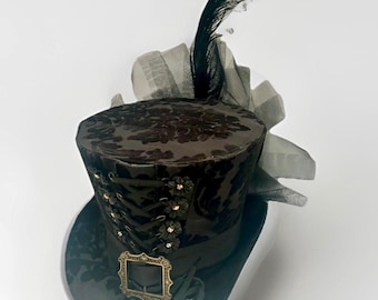 May include: A black top hat with a floral pattern, adorned with a black feather and a decorative buckle. The hat features a ribbon and floral accents, creating a vintage aesthetic. The hat is suitable for cosplay or themed events.