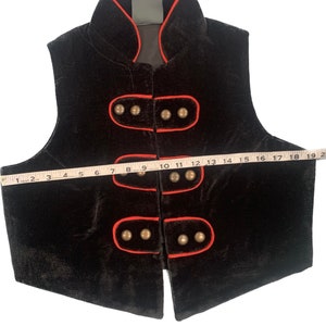 May include: Black velvet vest with a red trim and gold buttons. The vest has a mandarin collar and a straight hem.