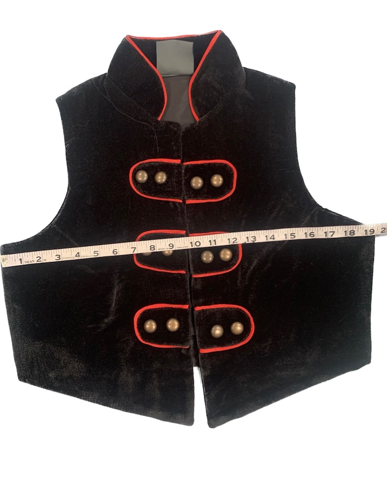 May include: Black velvet vest with a red trim and gold buttons. The vest has a mandarin collar and a straight hem.