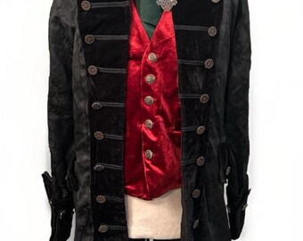 May include: A black velvet coat with ornate buttons and a high collar, paired with a red velvet vest. A green scarf and decorative brooch add detail to this gothic-inspired garment. The coat is displayed on a mannequin.
