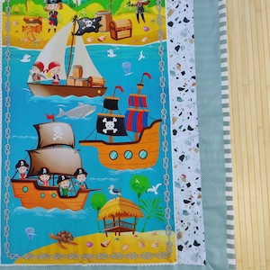 Op de afbeelding: Een kleurrijk stoffen paneel met een piratenthema, met cartoon illustraties van piratenschepen, schatkisten en piraten op een tropisch eiland. Het paneel heeft een blauwe achtergrond met een decoratieve rand en een lichtgroene rand.