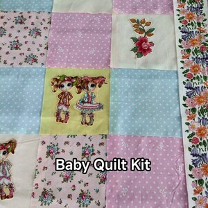 Peut inclure: Un kit de courtepointe pour bébé avec un patchwork. La courtepointe comprend des imprimés floraux, des pois et des illustrations de poupées. Le texte "Baby Quilt Kit" est affiché sur la courtepointe.