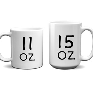 May include: Two white ceramic mugs with black lettering. The smaller mug says "11 oz" and the larger mug says "15 oz".