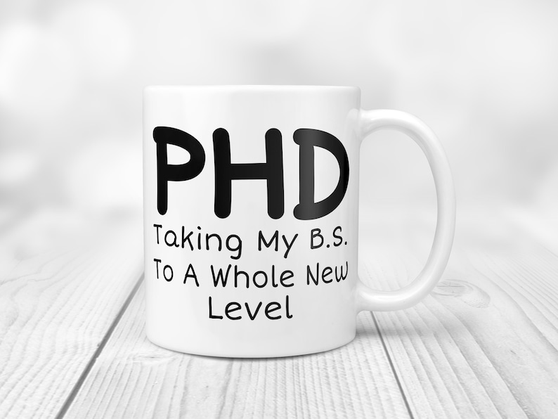 Puede incluir: Taza de caf&eacute; de cer&aacute;mica blanca con texto negro que dice "PHD Taking My B.S. To A Whole New Level".