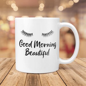 May include: White ceramic coffee mug with a black graphic of closed eyelashes and the text "Good Morning Beautiful".