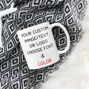May include: White ceramic mug with black text that reads "YOUR CUSTOM IMAGE/TEXT OR LOGO CHOOSE FONT & COLOR". The mug is sitting on a black and white patterned blanket.