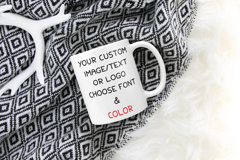 May include: White ceramic mug with black text that reads "YOUR CUSTOM IMAGE/TEXT OR LOGO CHOOSE FONT & COLOR". The mug is sitting on a black and white patterned blanket.