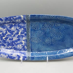 May include: A rectangular ceramic serving platter with a blue and white floral pattern. The platter is divided into two sections, one with a detailed floral design and the other with a raised leaf pattern. The platter is approximately 12 inches long.