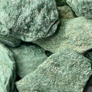 May include: A close-up of a pile of green aventurine stones. The stones are rough and have a sparkly, glittery texture.