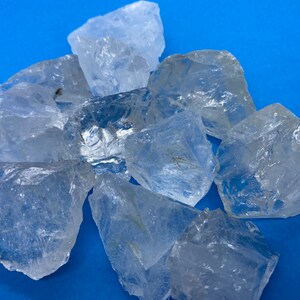 May include: A group of clear quartz crystals on a blue background. The crystals are various sizes and shapes, with some showing internal inclusions.