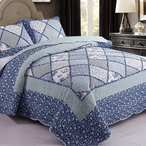 May include: A blue and white floral patterned quilt with a patchwork design. The quilt is on a bed with two matching pillows.