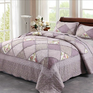 May include: A purple and white patchwork quilt with a floral pattern. The quilt is on a bed with two matching pillowcases.