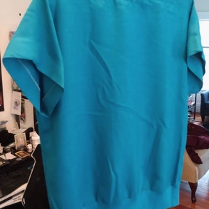 May include: A turquoise blue short-sleeved blouse with a scoop neck and a slightly gathered hem.