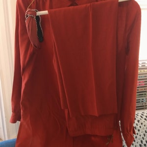 May include: A rust-colored blouse and pants set. The blouse has a collar and long sleeves. The pants have a straight leg.