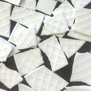 May include: A collection of irregularly shaped, white mosaic tiles with a diamond pattern. The tiles vary in size and shape, creating a textured surface. The mosaic pieces are scattered against a dark background.