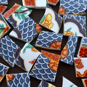 May include: A collection of broken ceramic tiles with various patterns. The tiles feature designs in blue, orange, red, and white, including floral motifs and geometric shapes. The fragments are scattered, showcasing the intricate details of the original artwork.